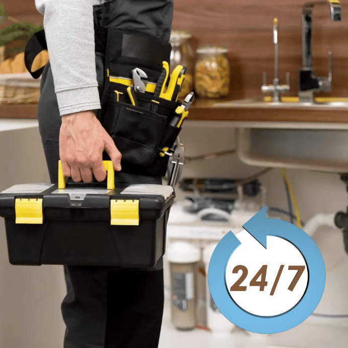 Technician in a tool belt carrying a yellow-handled toolbox in a workshop setting, with a 24/7 service badge nearby.