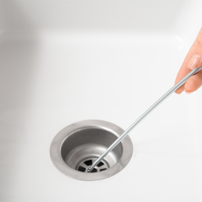 Person uses a metal plumbing auger to unclog a stainless steel sink drain.