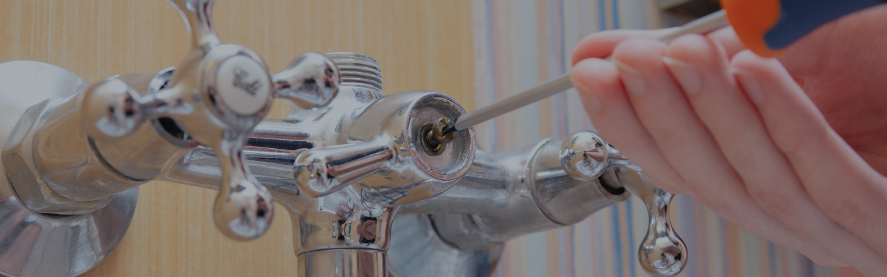 Close-up of a person using a screwdriver to tighten a chrome faucet valve in a bathroom setting.