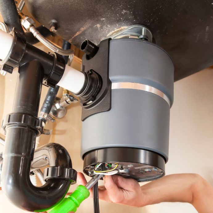 Under-sink garbage disposal being installed or serviced, with pipes and wiring exposed under a kitchen sink.