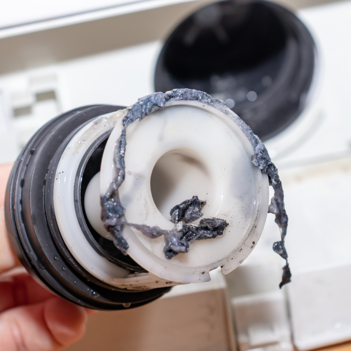 Close-up of a damaged plastic washer filter insert with melted seal and burnt debris attached.
