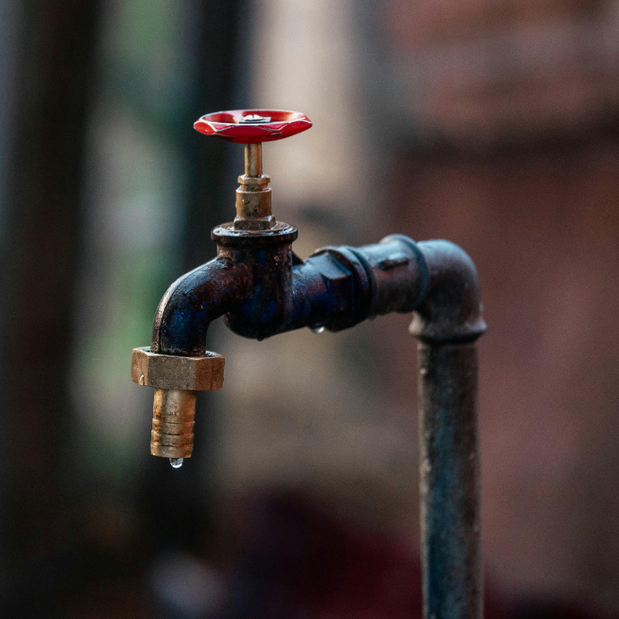 Copper outdoor faucet with a red handle, close-up showing a drip from the spout.