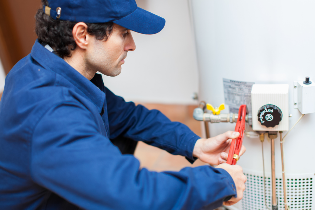 HVAC technician in a blue uniform tightening a valve on a heating system with a red wrench