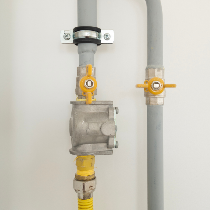 Gas line with yellow-handled valves and a metal regulator mounted on a wall.