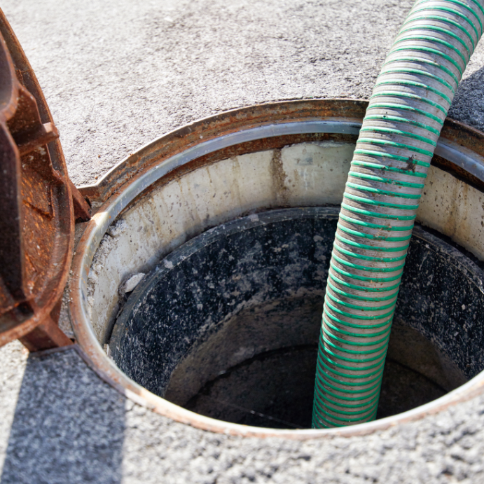 Open manhole with a green corrugated hose lowering into it during outdoor maintenance operation.