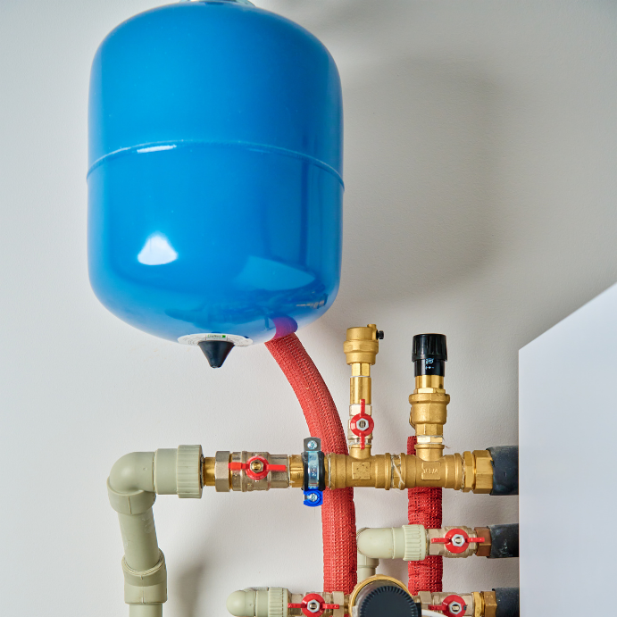 Blue expansion tank connected to brass valves and red hoses in a home water pressure system.