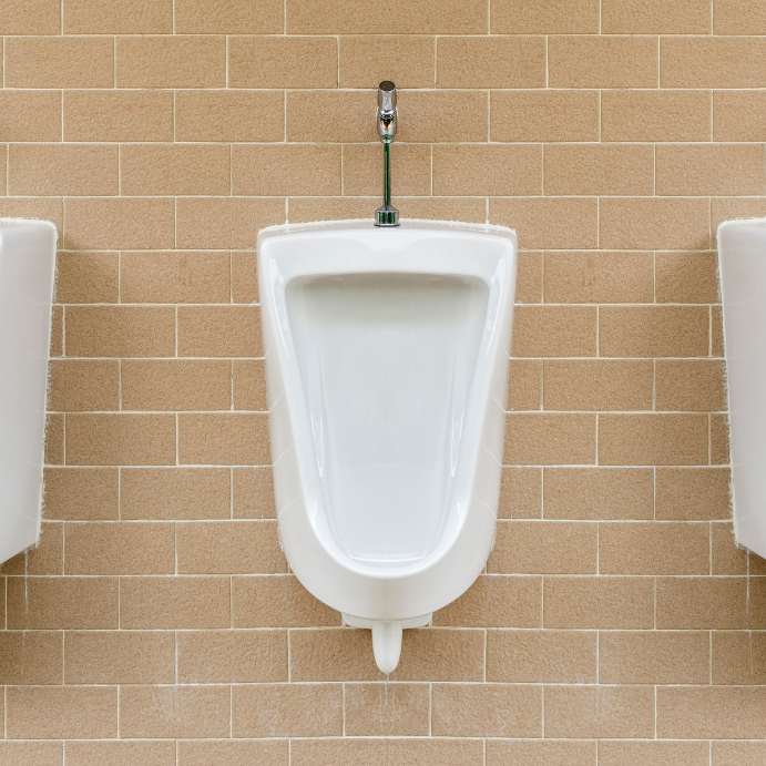 White porcelain urinal mounted on a tan tiled wall with a chrome flush valve above it.