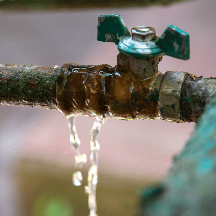Close-up of a rusty outdoor faucet with a green handle, water dripping from the valve.