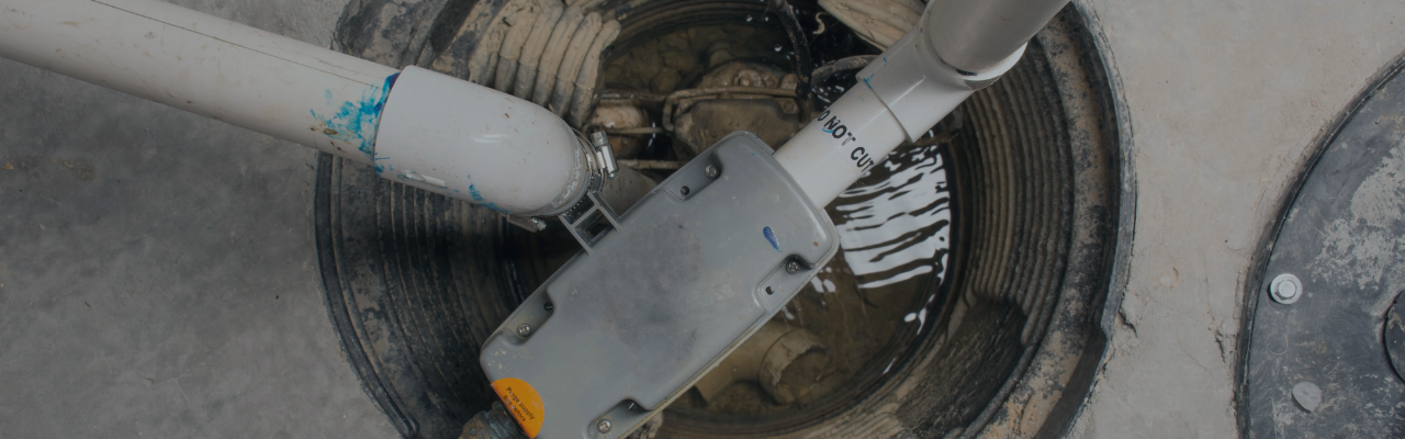 Industrial robotic arm entering an open manhole for sewer maintenance, with muddy water visible inside the shaft.