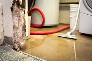 Wet floor in a laundry/utility area with a red hose, water heater, and washing machine nearby, suggesting a possible leak or spill.